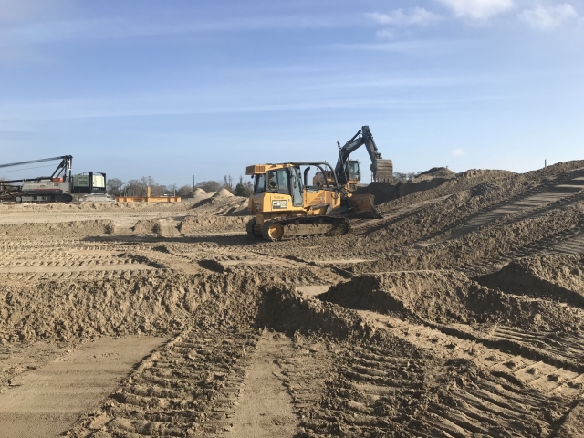 a large, sandy job site with a dozer and an excavator in the background
