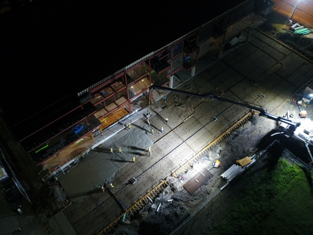 a top down view of workers pouring concrete late at night. it is dark and the jobsite is lit up by industrial lights.