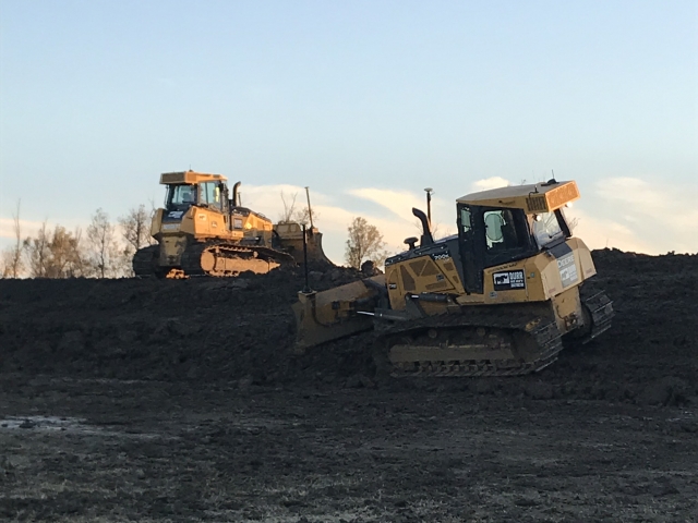 two skidsteers run across a levee