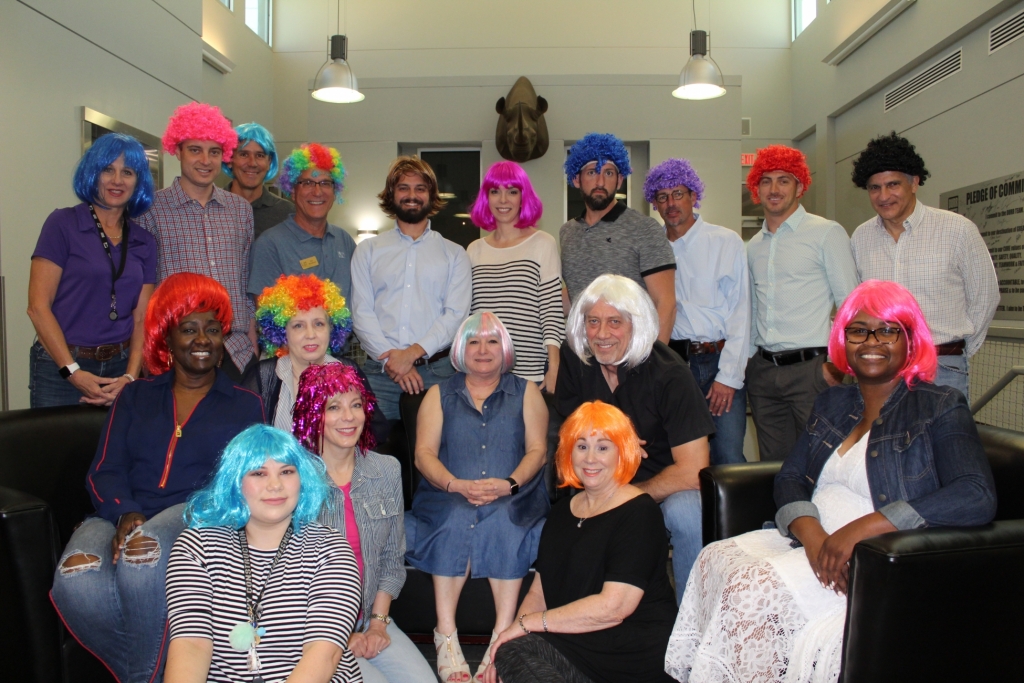 employees all have on colorful wigs as they pose for the camera in a group