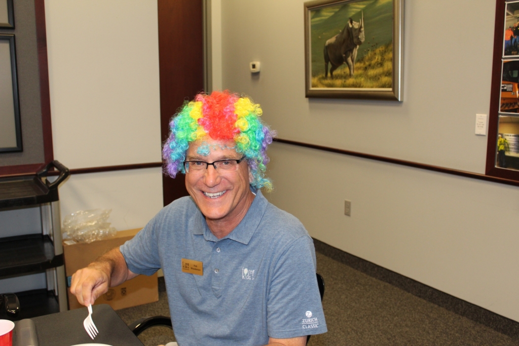 a worker in a rainbow wig smiles