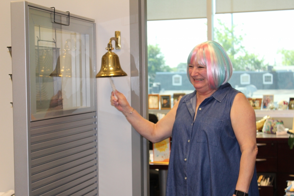 Jan, wearing a colorful wig, rings a bell signifying that she has beaten cancer