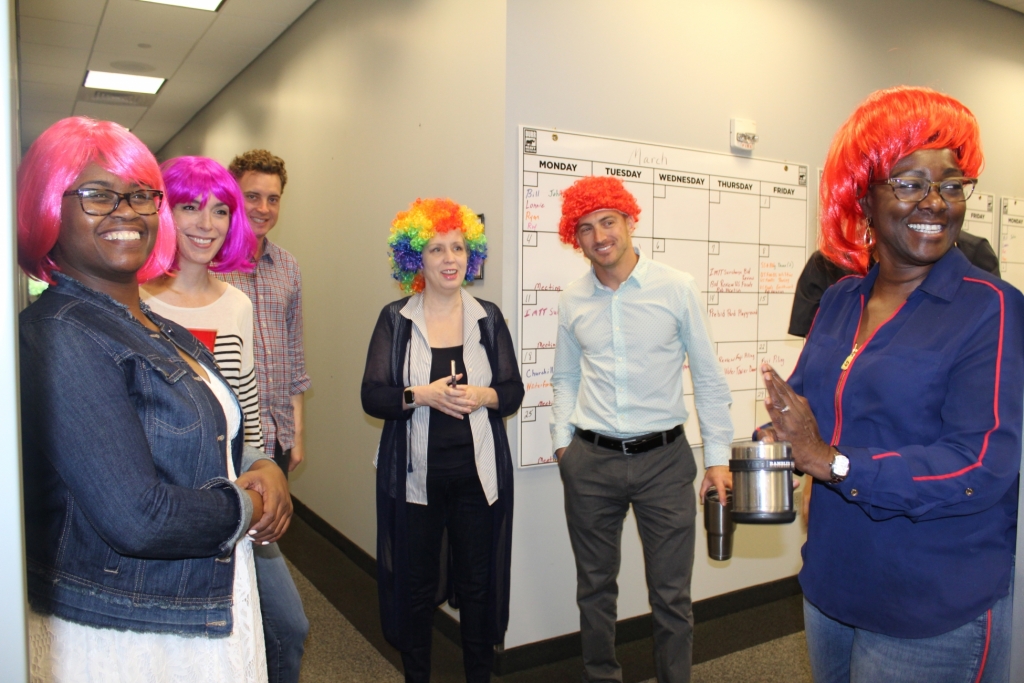 a group of workers in colorful wigs smile as they clap