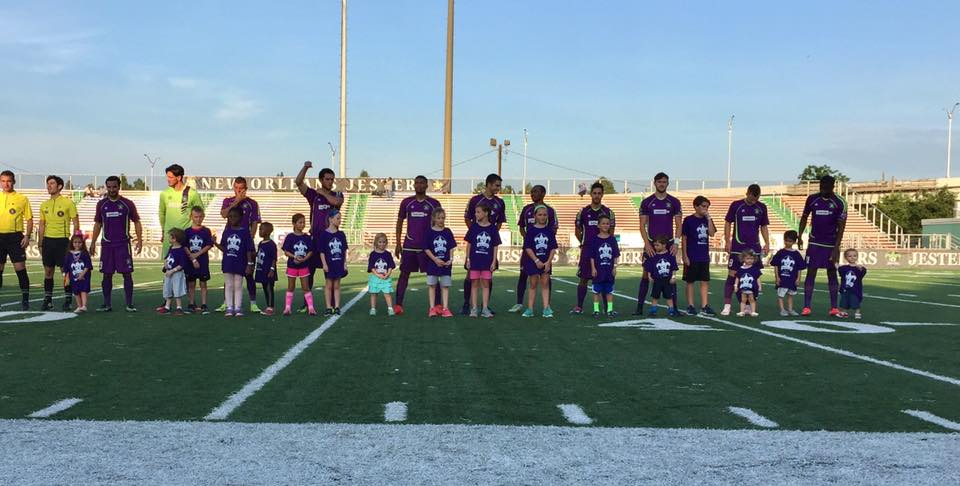 Players and kids standing for the National Anthem during a Jesters soccer game