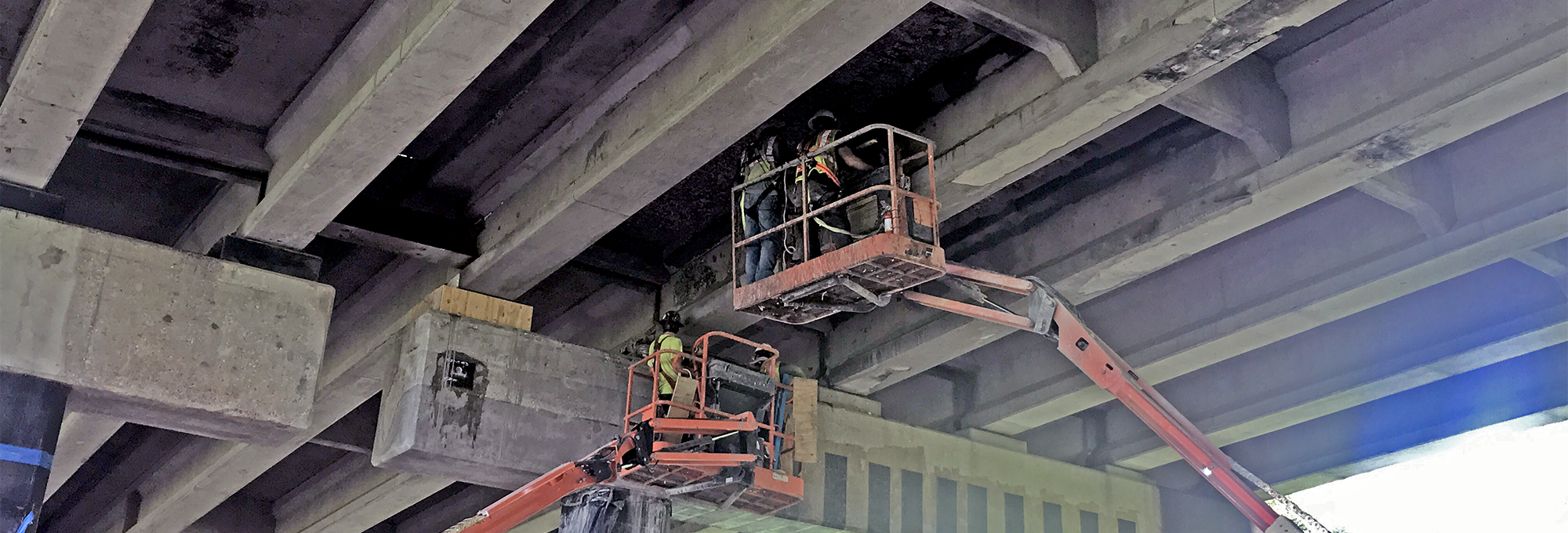 Workers stand on a lift underneath the bridge
